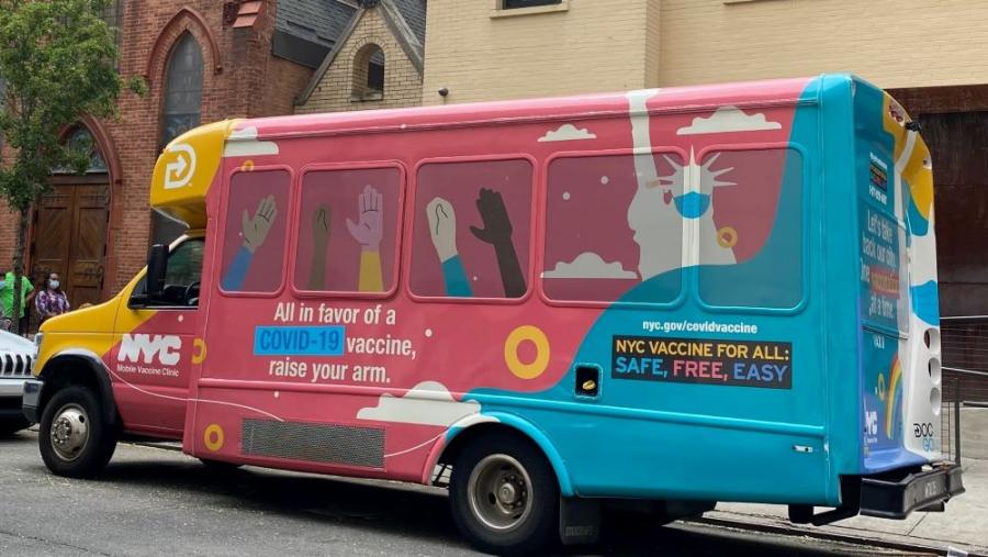A multi-colored vaccine van parked in front of a church in New York City.