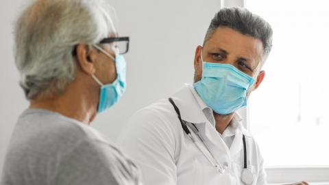 Un hombre que lleva un tapaboca visita con su médico, también usando un tapaboca
