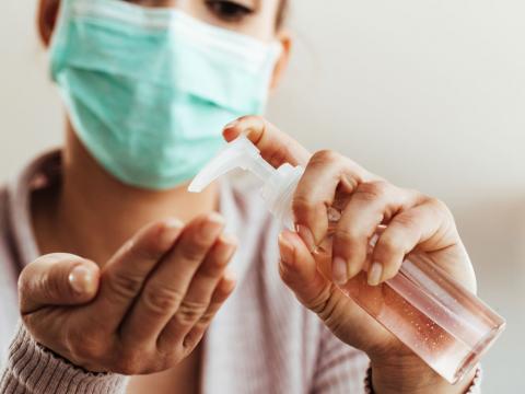 close up shot of a woman wearing a mask, using hand sanitizer